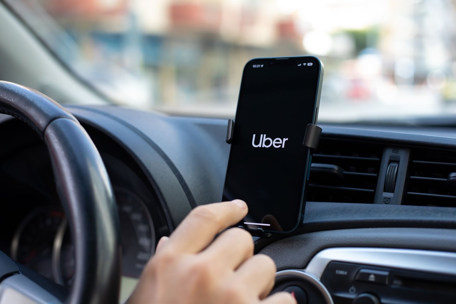 mão de pessoa boa clicando em celular acom logotipo da Uber afixado em painel de carro lista de carros Uber Black Uber Comfort 2025